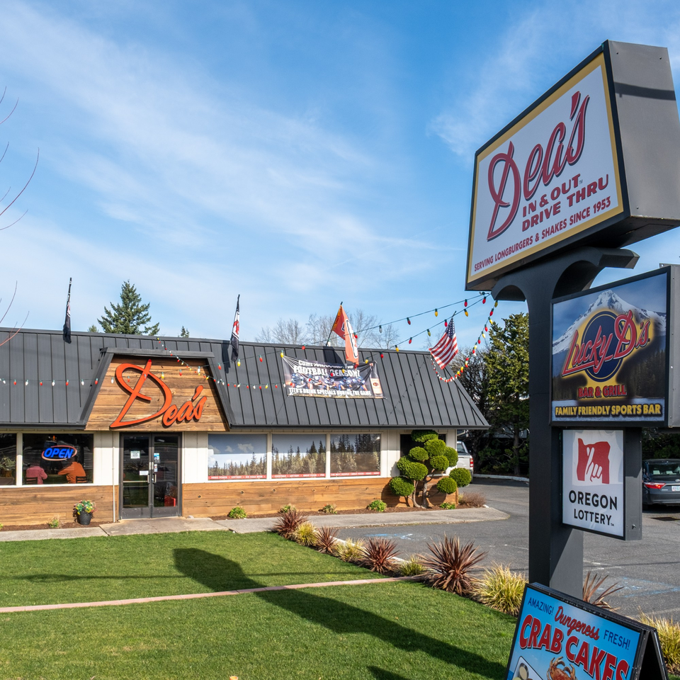 Exterior of Dea's In & Out restaurant with a large sign, drive-thru, and outdoor seating.