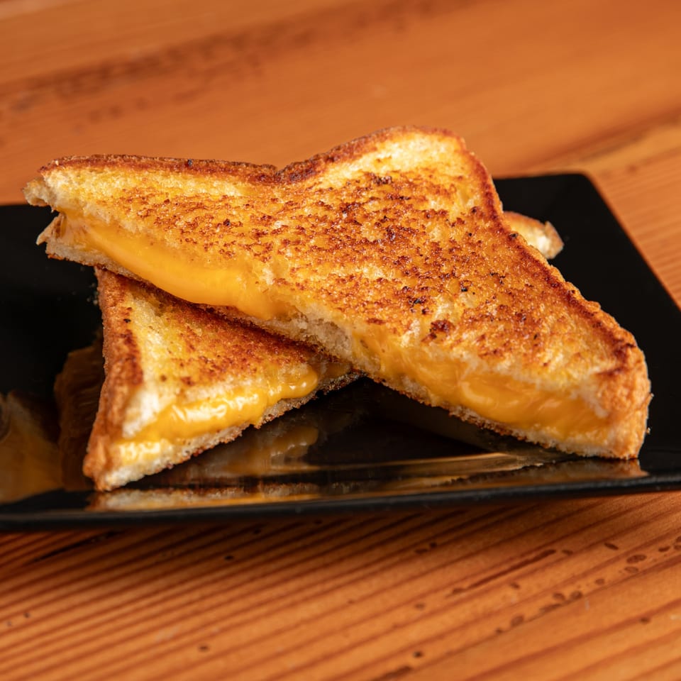 Dea's In & Out grilled cheese sandwich, cut in half, revealing melted cheese on a black plate.