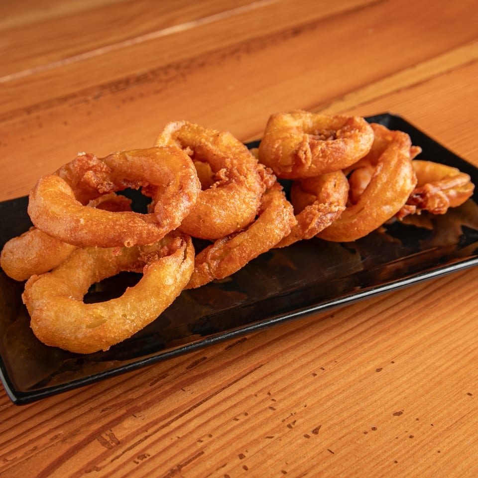 A black rectangular plate filled with golden-brown, crispy onion rings on a wooden table.