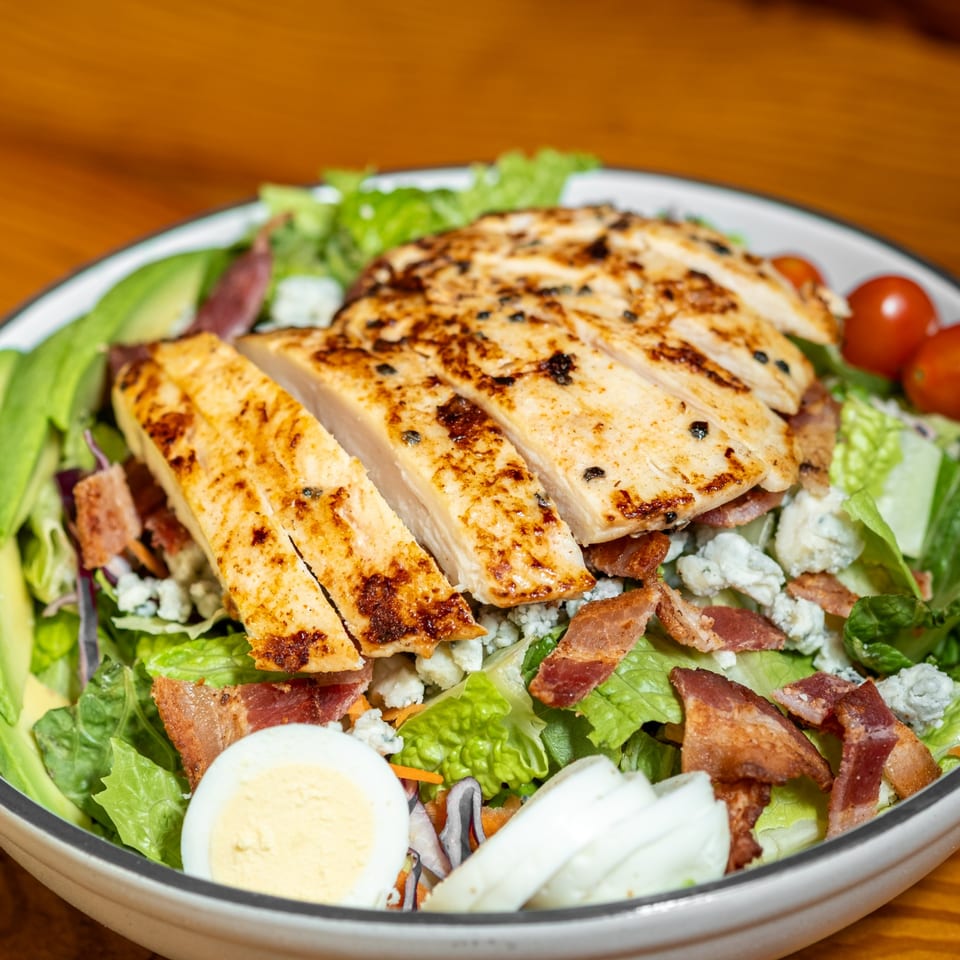 Grilled chicken salad with avocado, bacon, blue cheese, hard-boiled egg, and cherry tomatoes.