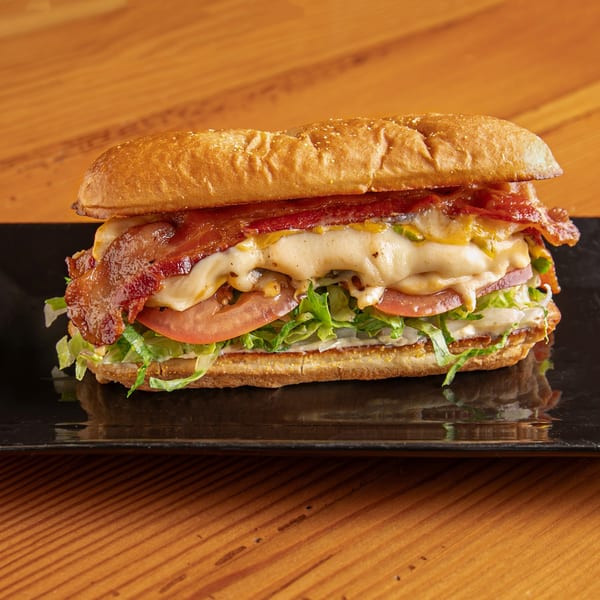 Dea's In & Out's bacon sub sandwich with melted cheese, lettuce, and tomato on a black plate.