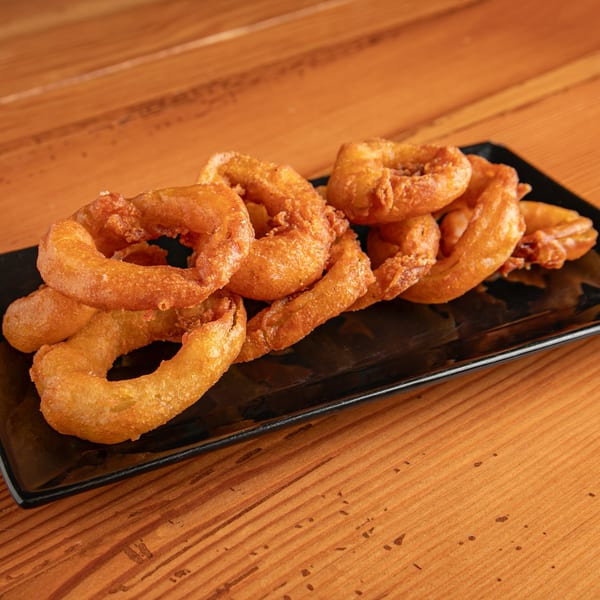 A black rectangular plate filled with golden-brown, crispy onion rings on a wooden table.