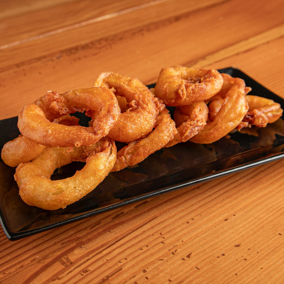 A black rectangular plate filled with golden-brown, crispy onion rings on a wooden table.