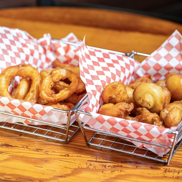 Two baskets of fried sides, one with onion rings and the other with fried mushrooms.
