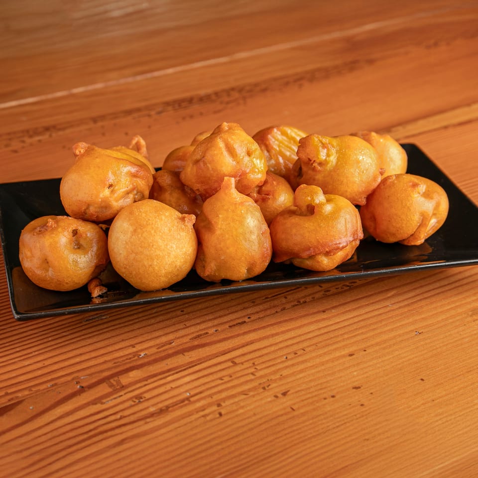 A black rectangular plate filled with golden-brown, irregularly shaped fried dough balls on a wooden table.