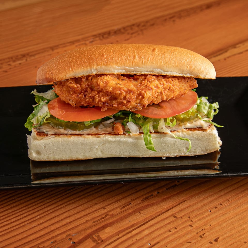 Dea's In & Out fried chicken sandwich with lettuce, tomato, pickles, and sauce on a bun.