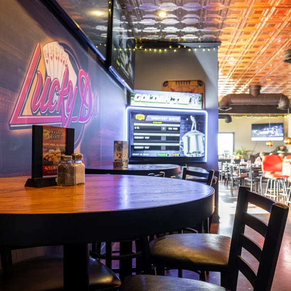 Interior of Dea's In & Out, with a "Lucky D's" neon sign, tables, chairs, and arcade games.