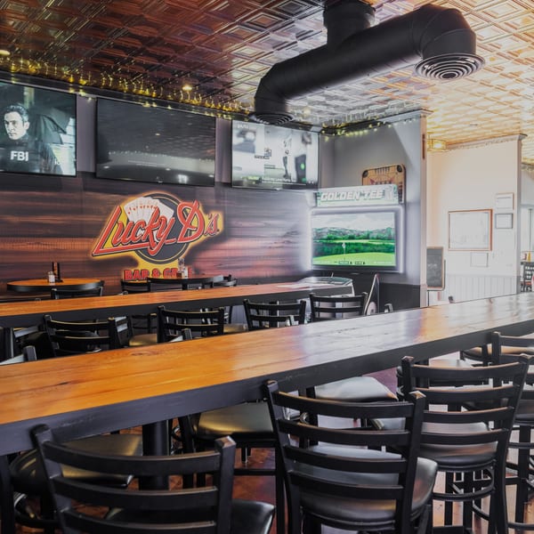 Interior of Dea's In & Out, a burger restaurant, with a long wooden bar, stools, and TVs.