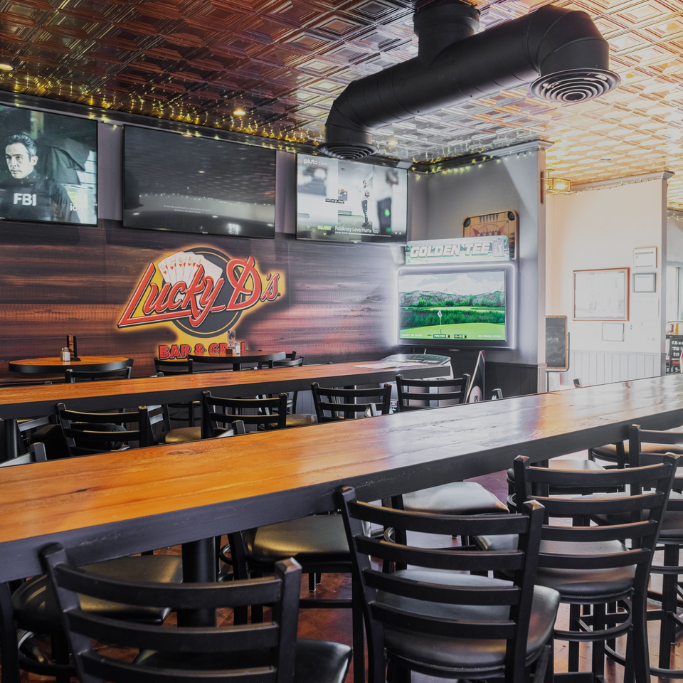 Interior of Dea's In & Out, a burger restaurant, with a long wooden bar, stools, and TVs.