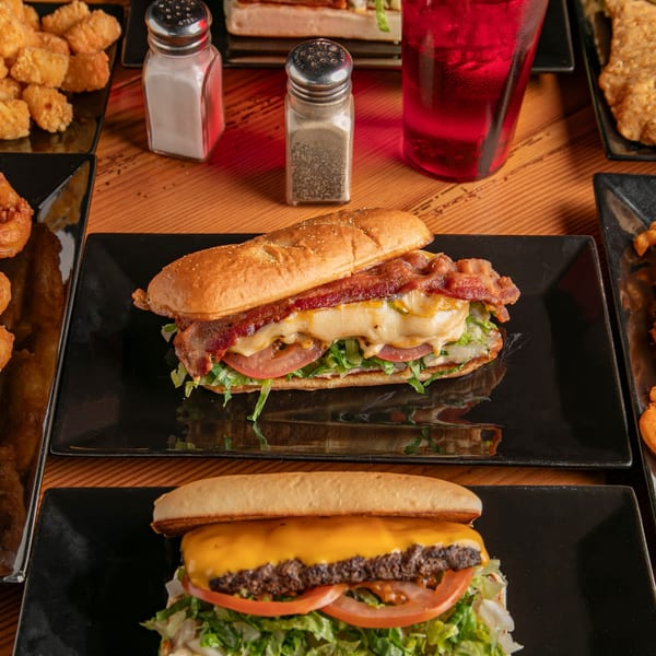 Dea's In & Out cheeseburger and bacon sub sandwich, with sides of tater tots and onion rings.